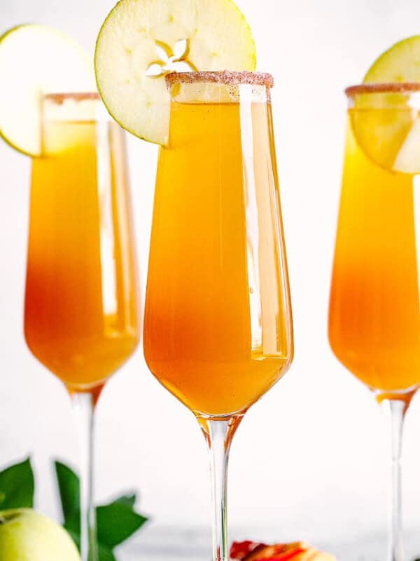 Apple Cider Mimosa in champagne flutes with apple slices.