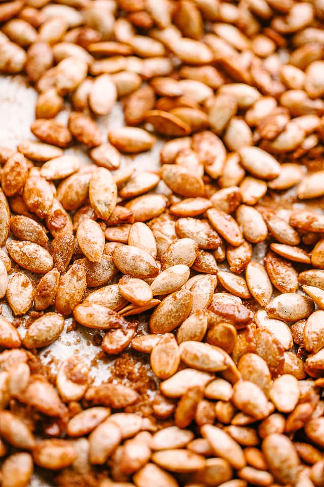 Roasted pumpkin seeds spread out on a baking sheet.