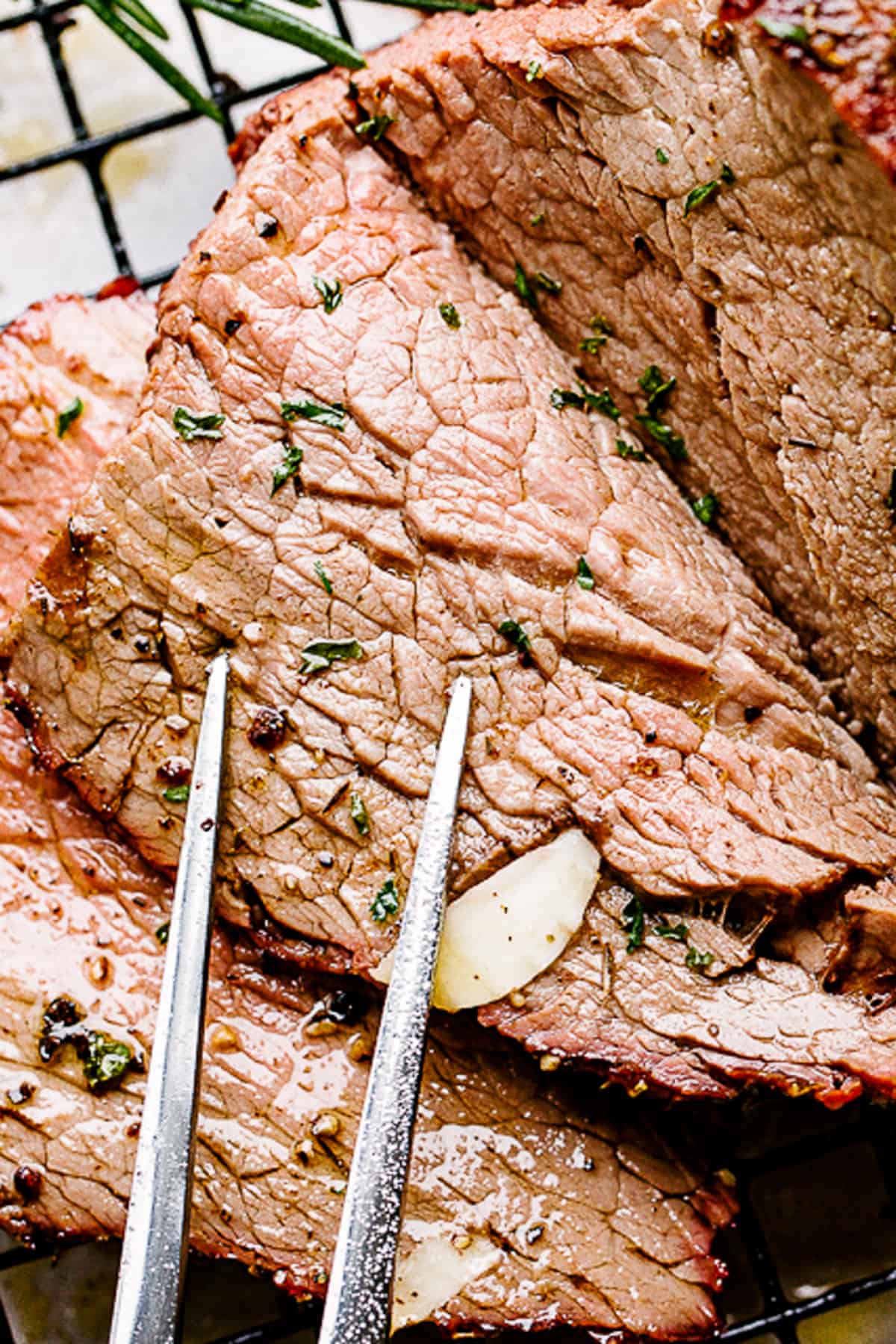 Up close shot of a slice of roast beef with a fork resting on top of the slice.