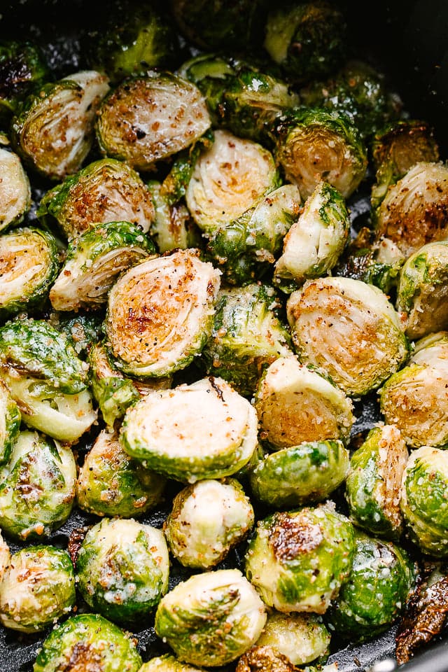 Halved, cooked brussel sprouts in a black air fryer basket.