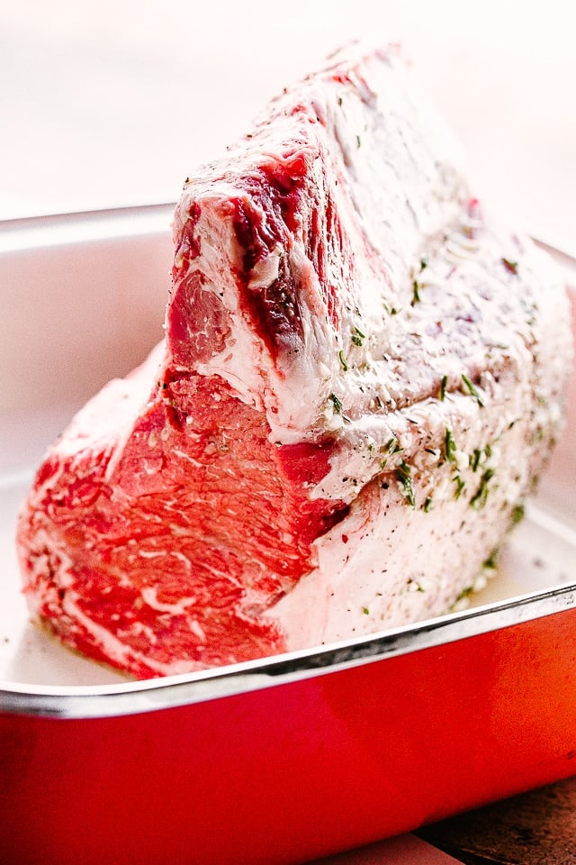 This juicy bone-in Prime Rib Roast with a garlicky crust and rich au jus is the ultimate holiday or special occasion centerpiece. Raw standing rib roast in a baking pan.