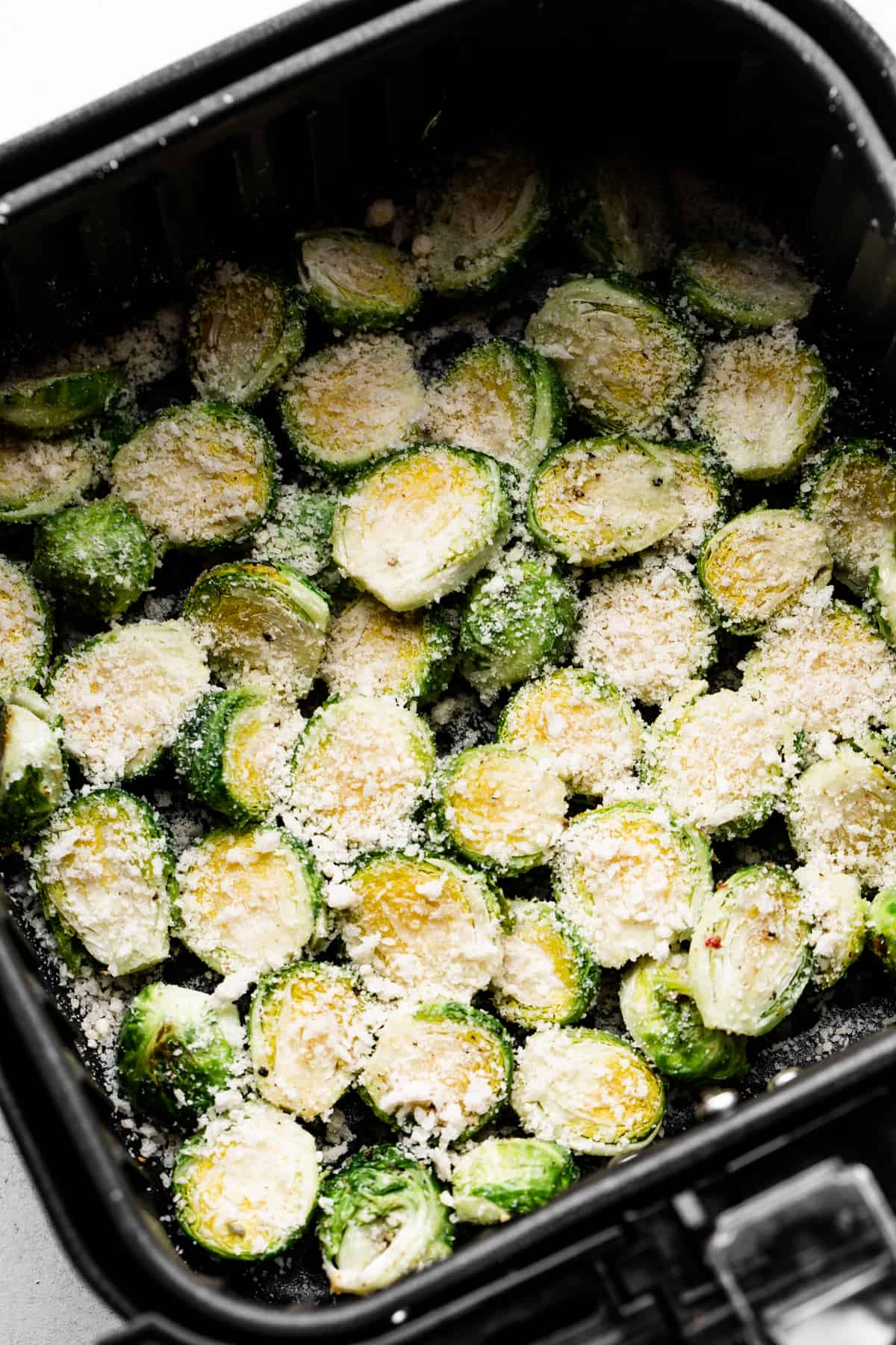 Raw brussel sprouts covered with parmesan in an air fryer basket