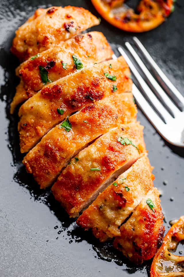 Fried chicken breast, sliced, and served on a dark plate next to a fork.