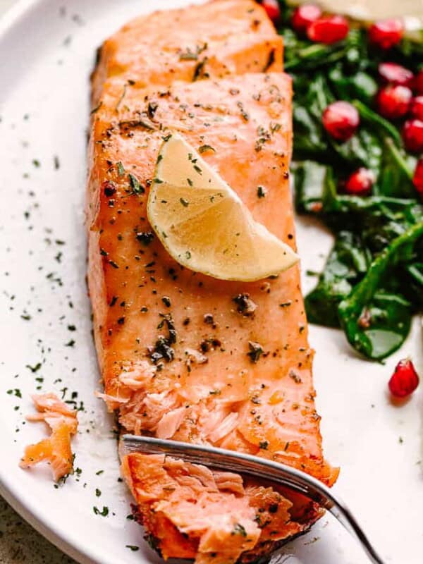 Salmon fillet garnished with lemon, on a plate with greens and pomegranate arils.