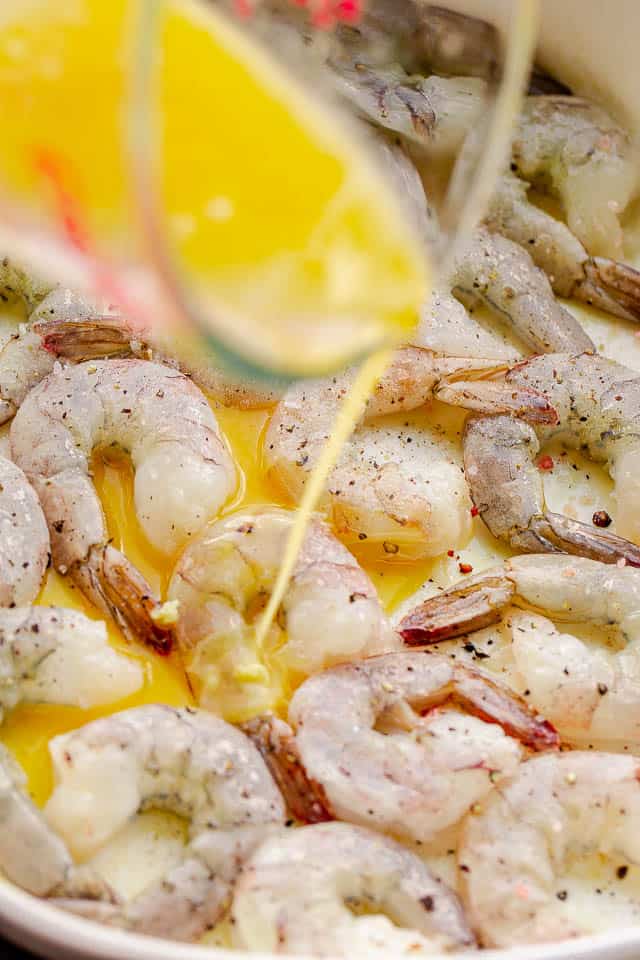 Pouring melted butter over raw shrimp in a baking dish.