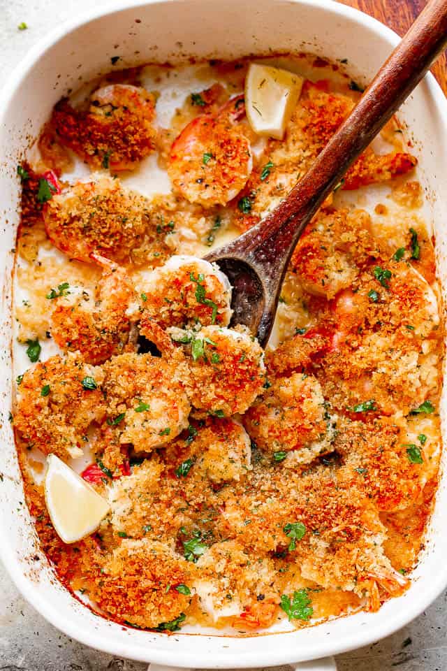 Spooning out shrimp scampi from a baking dish.