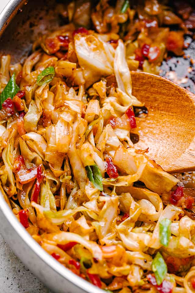 cooking cabbage and bacon in a skillet with a wooden spoon.