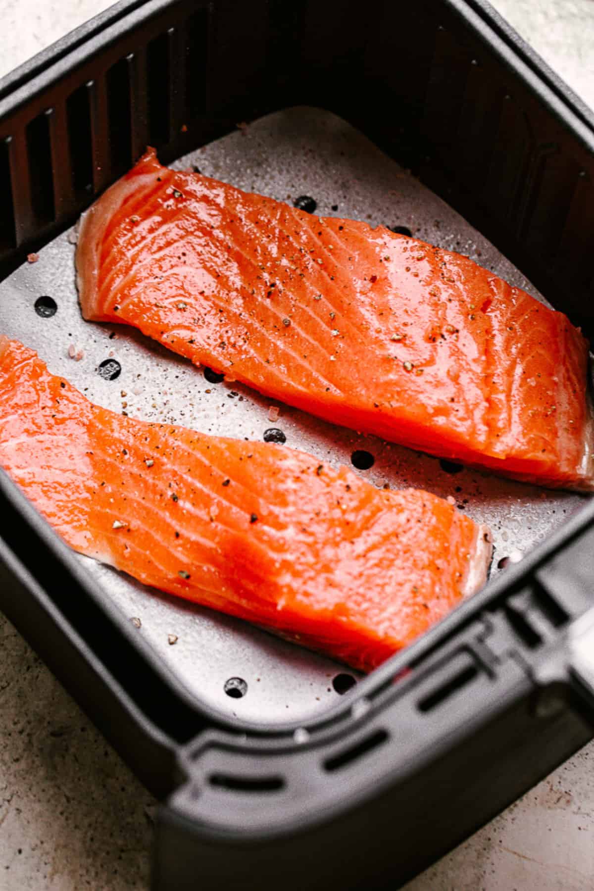 Two raw salmon fillets in an air fryer basket.