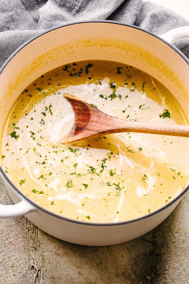 Overhead shot of creamy asparagus soup in a Dutch oven with a wooden spoon stirring through it.