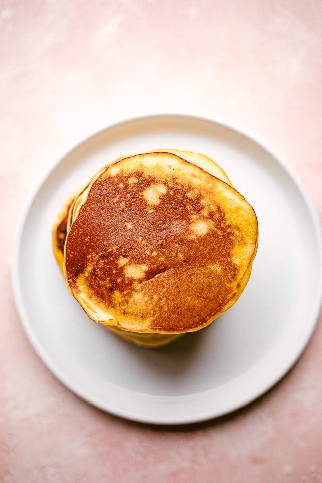 Overhead image of a stack of cooked pancakes set on a white plate.