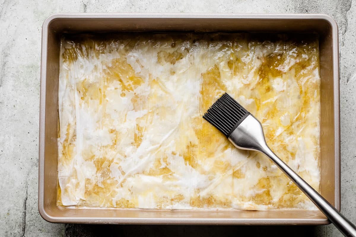 Brushing phyllo dough with butter in a baking sheet