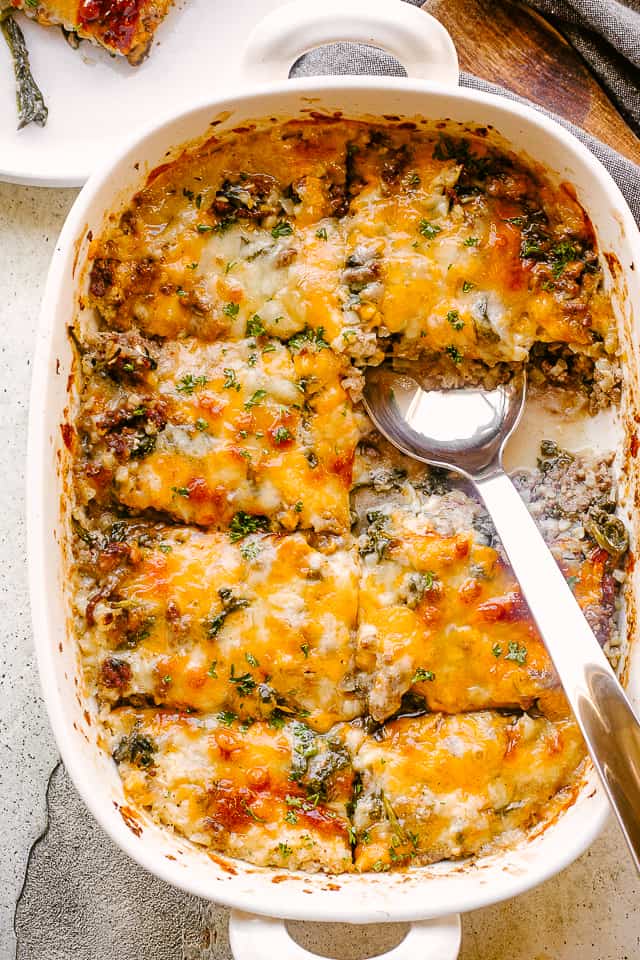 Serving cheesey ground beef cauliflower casserole in a white baking dish