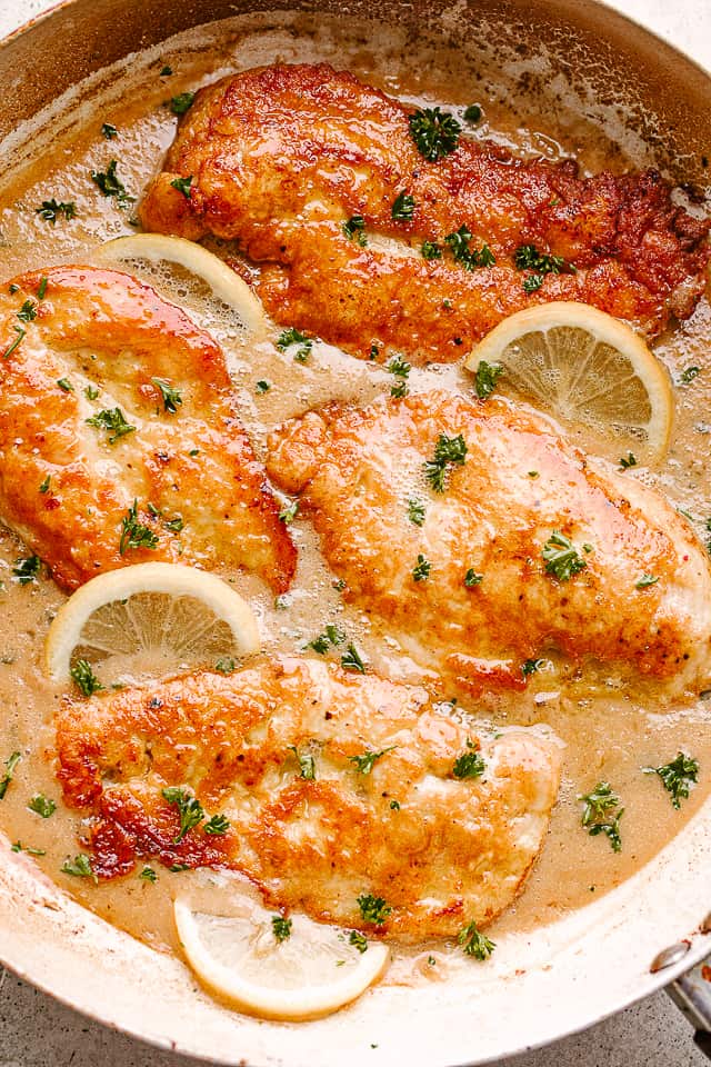 Chicken francaise in a skillet with lemon cream sauce, topped with lemon slices and fresh herbs.