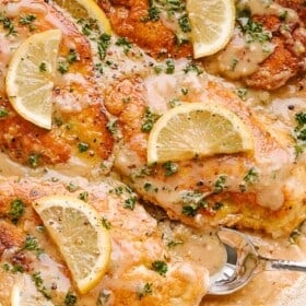 Chicken francaise in a skillet with lemon cream sauce, topped with lemon slices and fresh herbs.