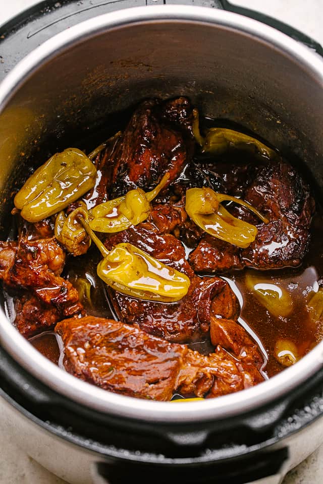 A pot roast cooking in an Instant Pot with pepperoncini arranged over the top of the beef.