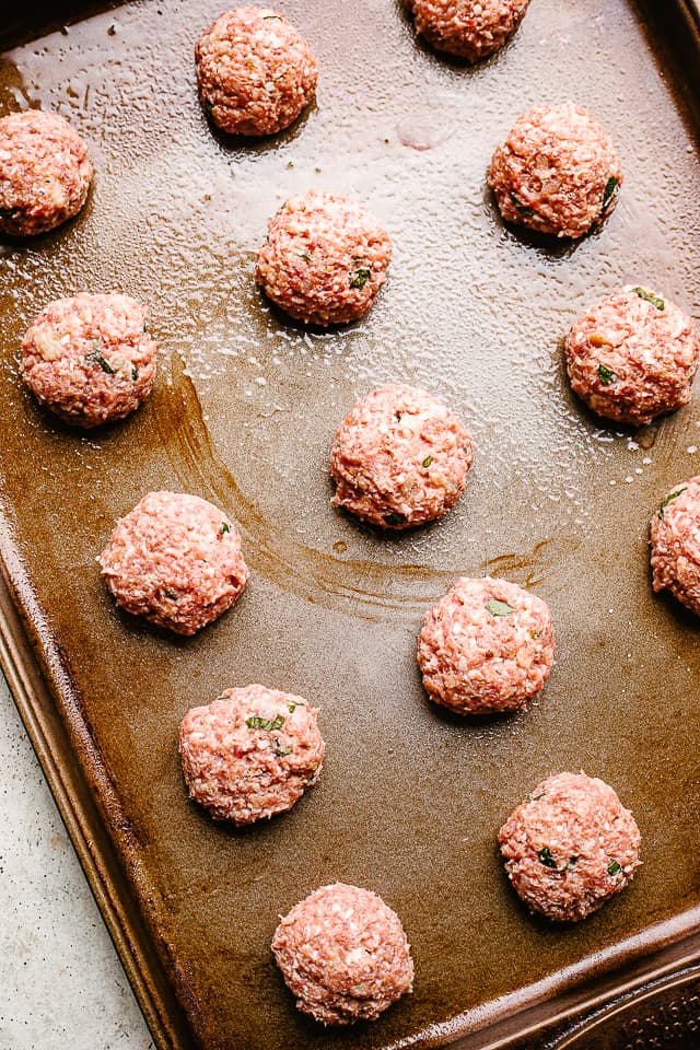 Meatballs rolled out and set on a pan before baking.