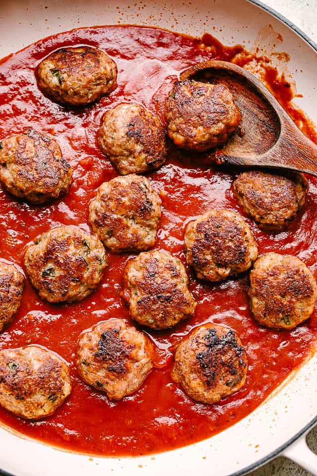 Baked meatballs are added to a pan of marinara sauce.