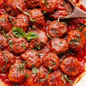 Baked meatballs in a pan with marinara and topped with fresh basil