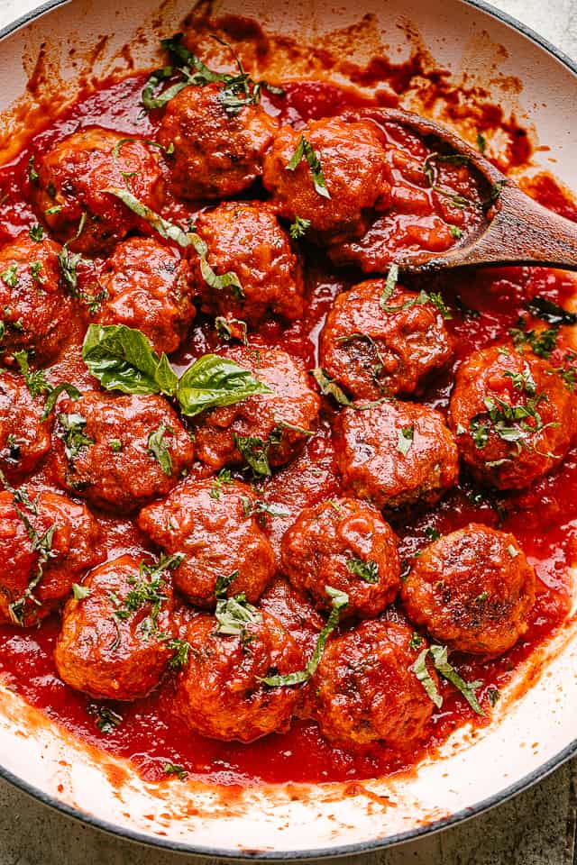 Baked meatballs in a pan with marinara and topped with fresh basil