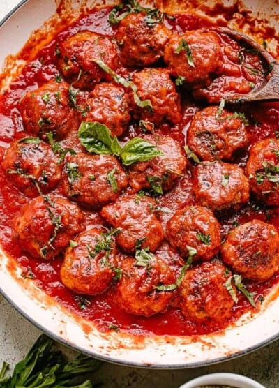 Meatballs in a pan with tomato sauce and topped with basil.