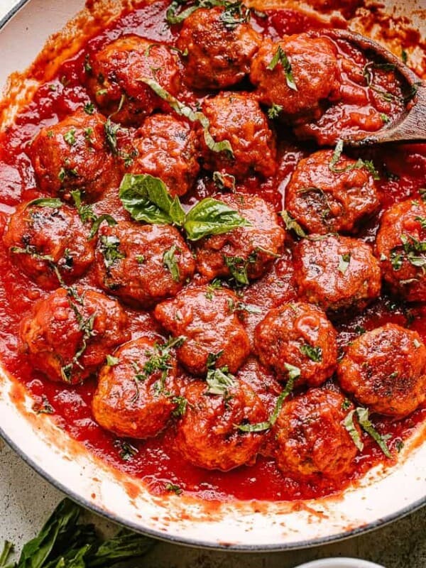 Meatballs in a pan with tomato sauce and topped with basil.