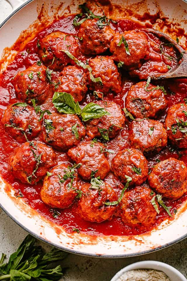 Meatballs in a pan with tomato sauce and topped with basil.
