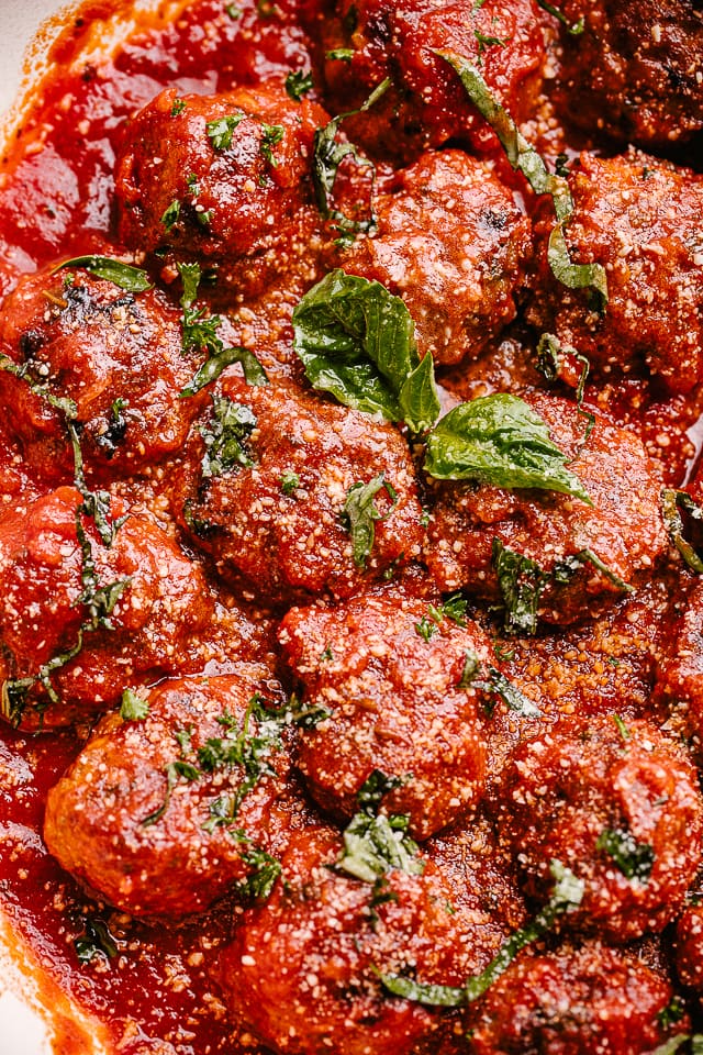 Close-up image of meatballs stirred in with marinara sauce and garnished with fresh basil leaves.