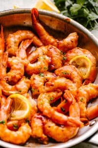 Skillet barbecue shrimp in a pan garnished with lemon wedges and parsley