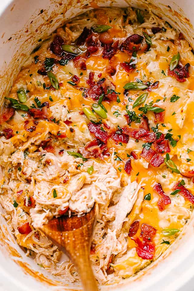 Slow cooker crack chicken topped with bacon and herbs and being stirred