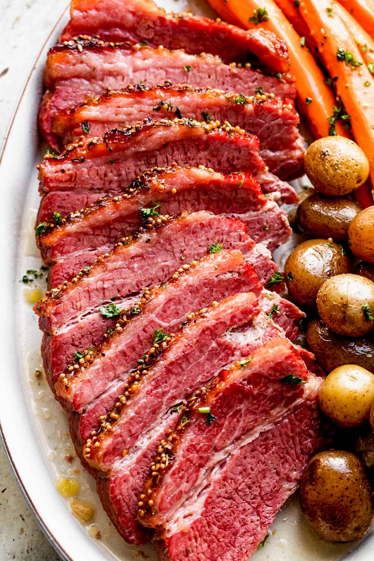 overhead shot of slow cooked and sliced corned beef, and served with small potatoes and long carrots.
