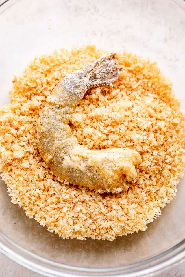 A shrimp being dredged in panko bread crumbs.