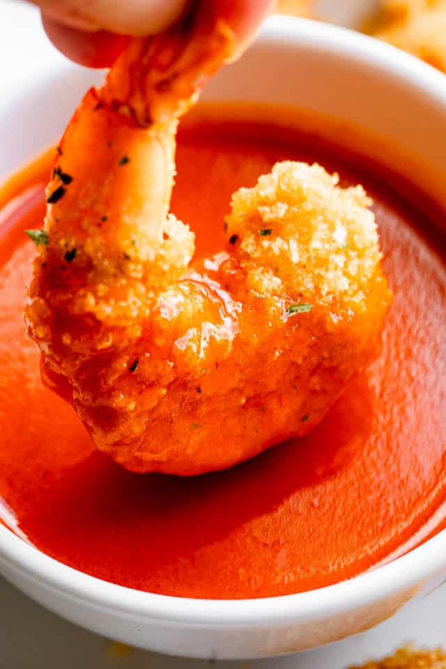 A single air fryer shrimp being dipped into Buffalo sauce. 