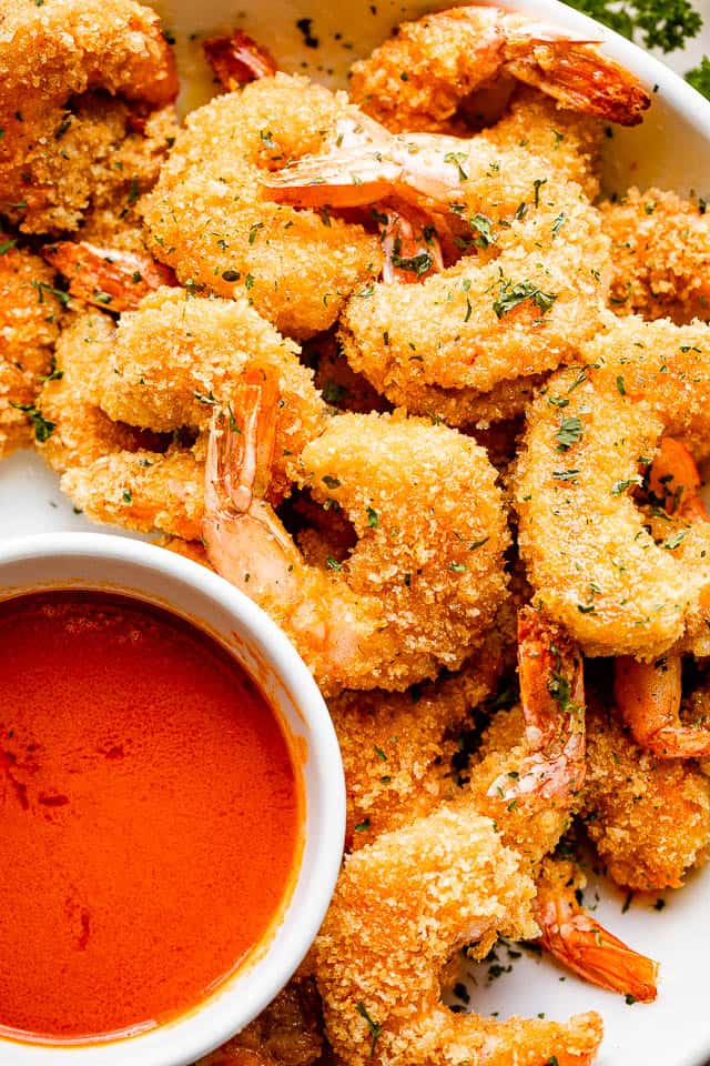 A plate of air fryer shrimp topped with parsley and Buffalo sauce on the side.