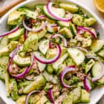 A bowl filled with flaky tuna, avocado, cucumbers, and red onions.