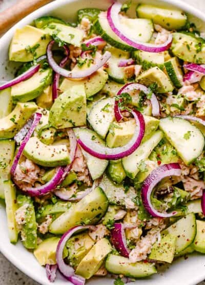 avocados, tuna, and cucumbers in a salad bowl garnished with red onions