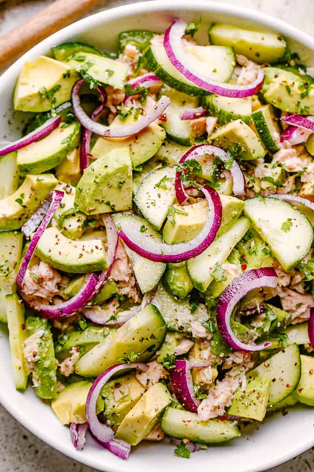 avocados, tuna, and cucumbers in a salad bowl garnished with red onions