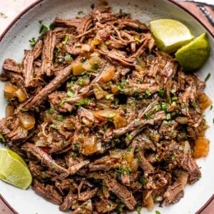 pulled beef barbacoa served in a bowl with lime wedges