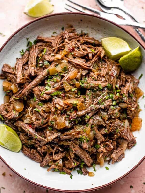 pulled beef barbacoa served in a bowl with lime wedges