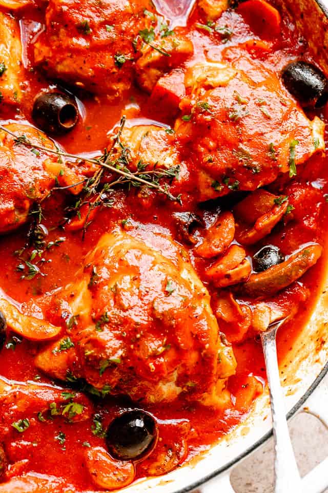 Chicken pieces topped with fresh herbs and black olives in a large pot ready to be served. 