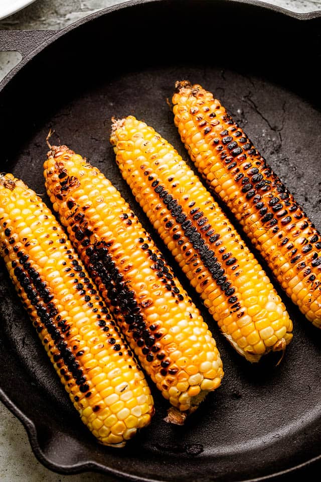 Four ears of corn charring in a cast iron skillet.