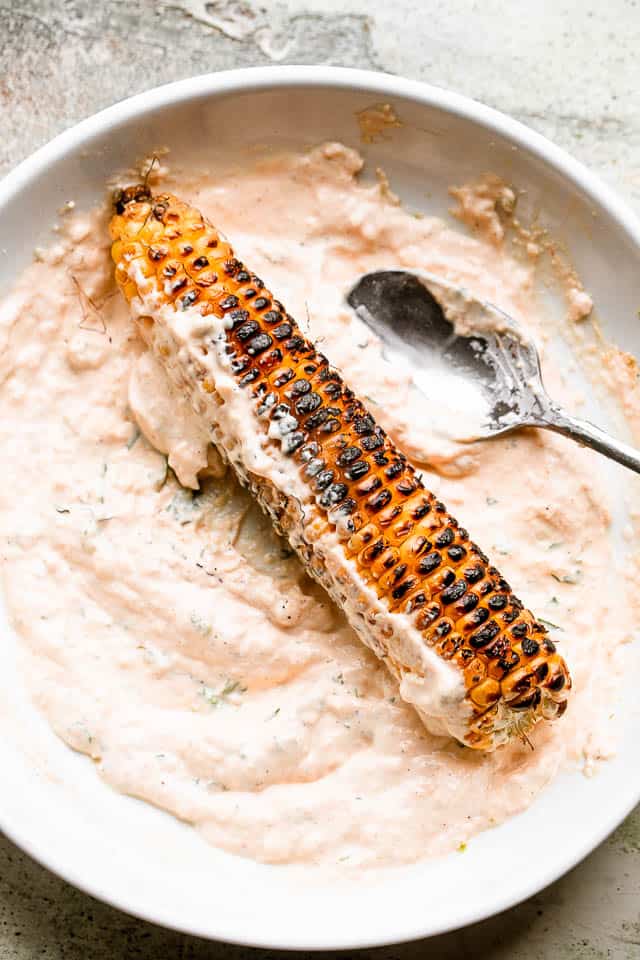 Charred corn on the cob placed in a mayo mixture.