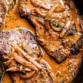two steaks in a cast iron skillet topped with onion gravy