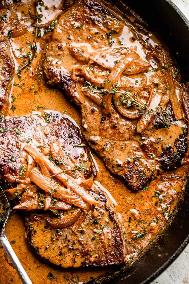 two steaks in a cast iron skillet topped with onion gravy