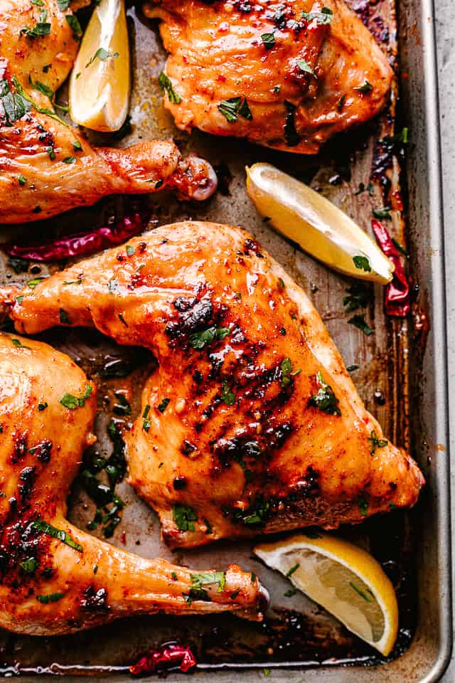 Roasted chicken legs arranged on a sheet pan. Lemon wedges are scattered around the chicken.