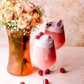 Two glasses of rosé sorbet floats garnished with raspberries next to a vase with Mother's Day flowers.