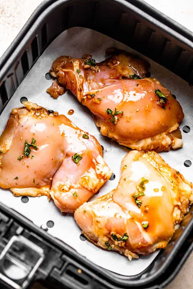 Boneless raw chicken thighs in an air fryer.