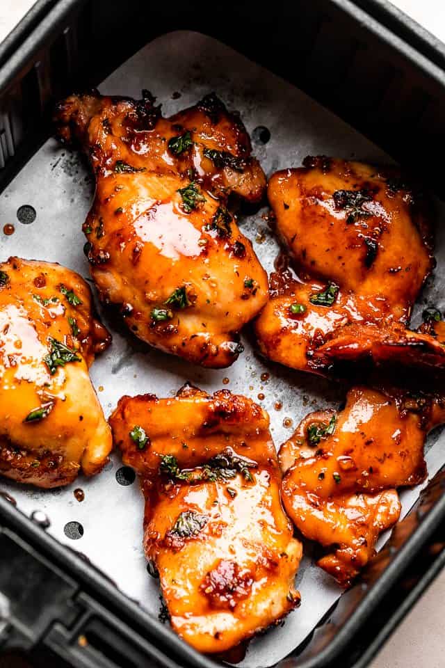 Cooked chicken thighs in an air fryer basket.