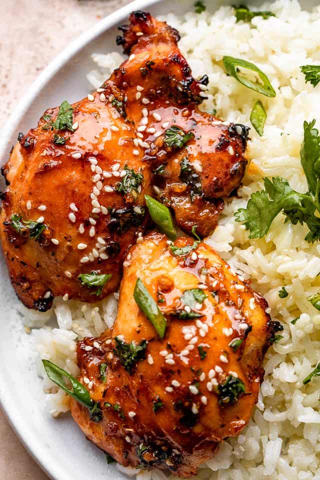 Top view of two glazed chicken thighs topped with sesame seeds and green onions, and served over white rice.