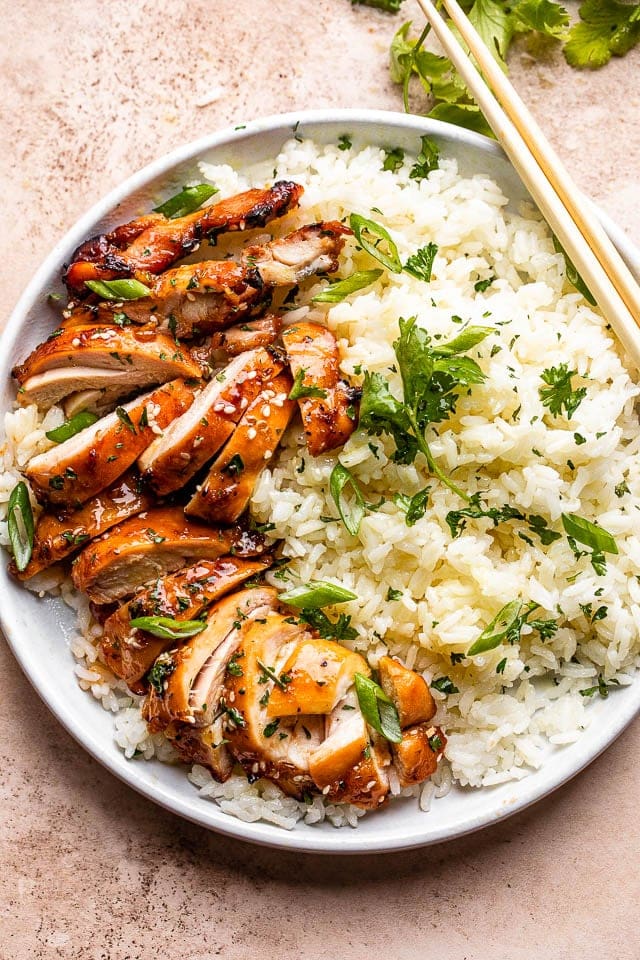 Boneless air fryer chicken thighs cut up and served on a plate with rice.