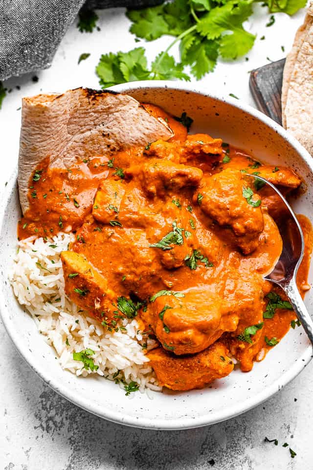 Chicken tikka masala in a bowl with rice and naan and a metal spoon.